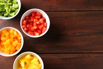 Pieces of fresh colorful bell peppers in bowls on wooden table, flat lay. Space for text