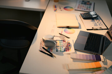 Creative designer workspace with color charts, laptop, headphones, and swatches for graphic design