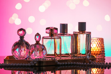 Many different perfume bottles and accessories on mirror surface against pink background with...