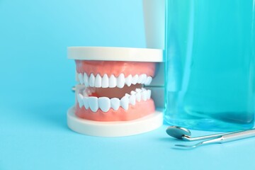 Different oral care products and dental model on light blue background, closeup
