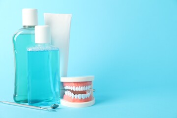 Different oral care products and dental model on light blue background. Space for text