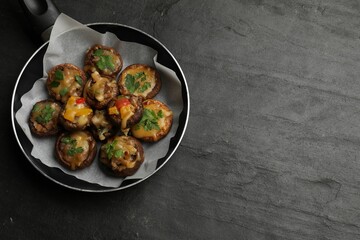 Tasty stuffed mushrooms in frying pan on black table, top view. Space for text