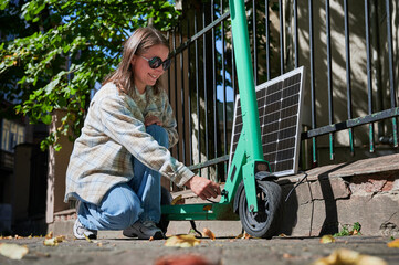 Woman connecting solar panel to electric scooter, highlighting practical application of sustainable renewable energy. Concept of integration of eco-friendly technology in everyday transportation.