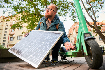 Man connects solar panel to electric scooter for charge, highlighting practical application of sustainable renewable energy. Concept of integration of eco-friendly technology in urban transportation.