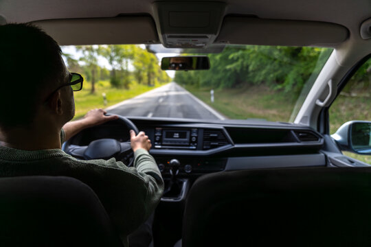 Driver at wheel. Forest road in spring. Front seat view.