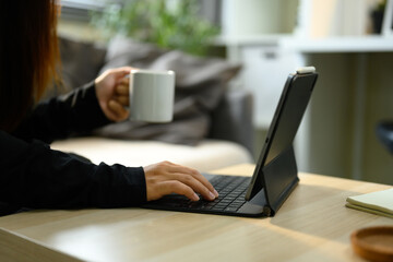 Close up of person holding a white coffee mug typing on a tablet keyboard while