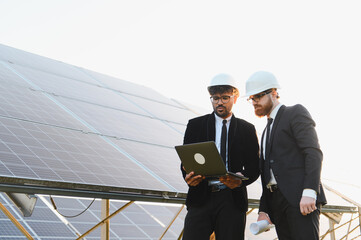 Engineers using laptop analyzing solar panel farm for renewable energy