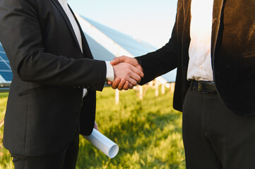 Engineers shaking hands in front of solar panels in sustainable energy project