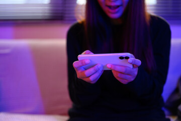 Young woman excited while playing mobile game with vibrant colored lighting