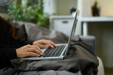 Side view of freelancer types on a laptop while resting on a sofa