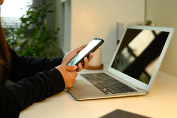 Close up shot of woman using smartphone at work desk with laptop