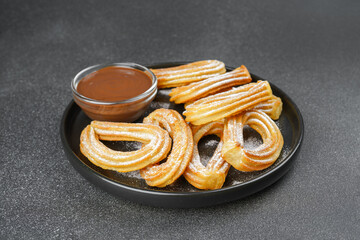 Traditional spanish dessert churros, fried dough pastry dusted with powdered sugar and chocolate sause on black background. Street food, sweet snack, homemade dessert.