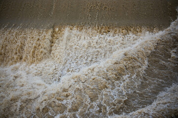 A turbulent, overflowing river in Florence, Italy. The water gushes over the rapids, creating foam and spray