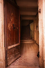 Fototapeta premium An open wooden door of an old house, a front entrance with steps that have seen better days and are worn out by time. A dark staircase leading upstairs, shabby walls, a worn old wooden door