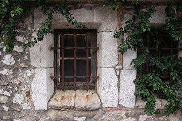 Old town, stone building, window closed with bars. Rusty forged bars and ivy growing on the walls. Window of an old house close-up