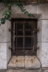 Old town, stone building, window closed with bars. Rusty forged bars and ivy growing on the walls. Window of an old house close-up