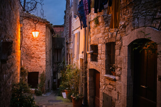 Fototapeta Evening old town Vence in France. Narrow cozy street with yellow vintage lantern that illuminates the road and clothes drying outside. Stone residential buildings
