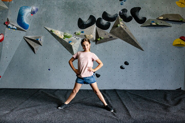 Young girl standing with legs wide open on the crash pad in an indoor rock-climbing gym.