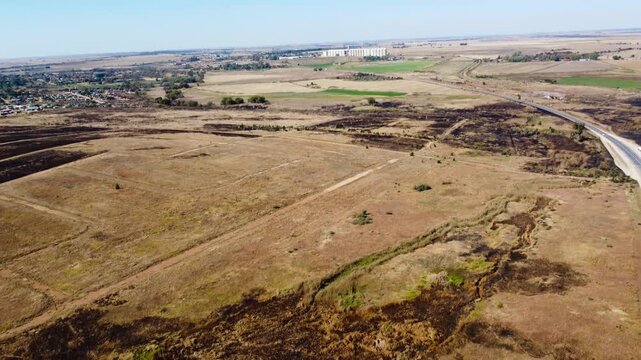 Camera panning up over dry brown agricultural land and grain silos in the distance 4K Aerial Video