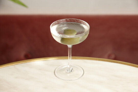 A glass of Martini with green olive on a marble surface