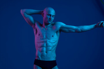 Obraz premium Athletic man posing in vibrant lighting, showcasing strong physique and confident expression. The image captures a playful and dynamic moment in a visually striking setting.