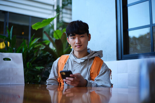 Young Asian delivery guy sitting with a food package on the table.