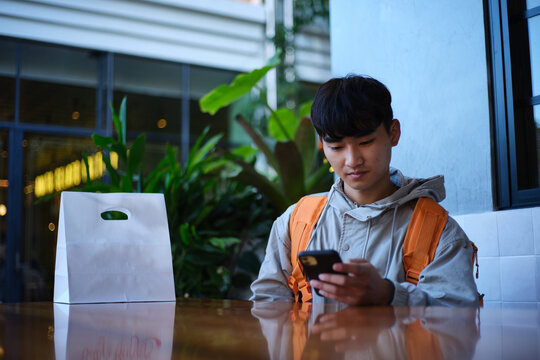 Young Asian delivery guy sitting with a food package on the table.