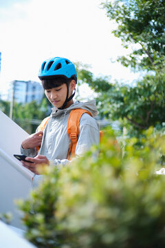 Young Asian delivery guy looking on his phone outdoors.