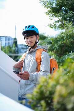 Young Asian delivery guy wearing helmet and insulated bag while holding his phone