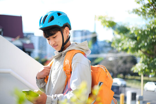 Young Asian delivery guy looking on his phone outdoors.
