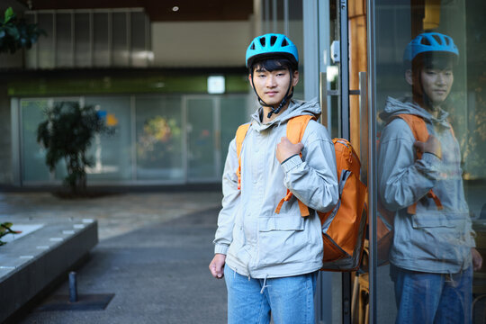 Young Asian delivery guy standing outside restaurant with cooler bag backpack