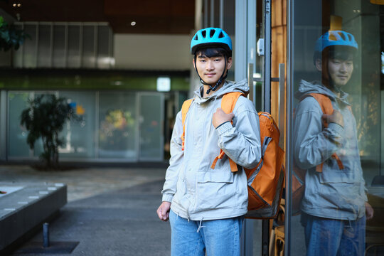 Young Asian delivery guy standing outside restaurant with cooler bag backpack