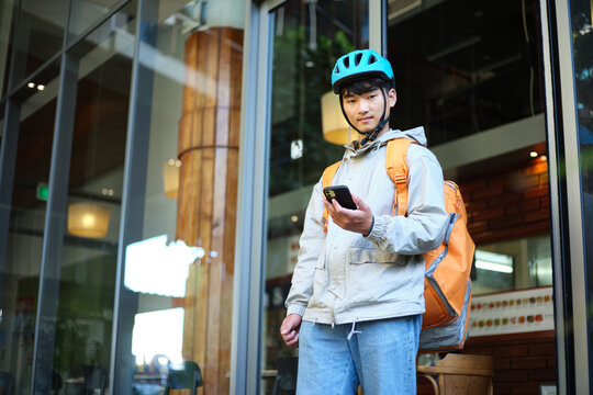 Asian delivery guy walking out of the restaurant while on his phone.