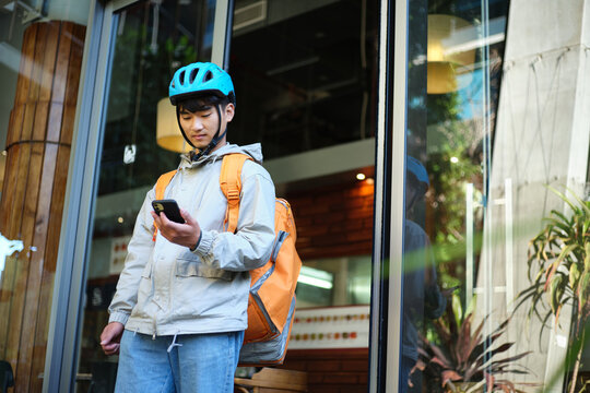 Asian delivery guy walking out of restaurant while on his phone
