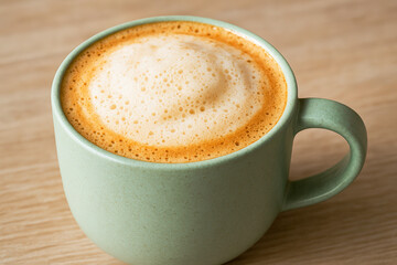 Obraz premium Freshly Brewed Latte in a Matte Green Ceramic Mug with Creamy Foam – A Cozy, Minimalist Coffee Moment Captured in Soft Natural Light on a Wooden Table, Perfect for Café Culture, Morning Ritual Imagery