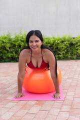 Latin woman doing pilates exercises with swiss ball outdoors