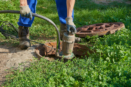 pumping water from a cesspool, a man holds a vacuum pump over a cesspool, pumping out a home septic tank with a pump