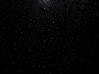 Raindrops on a dark car hood reflecting city lights. Abstract night shot resembling a starry sky with moisture and sparkle.