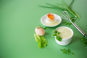 Homemade mayonnaise with herbs and eggs on a green background