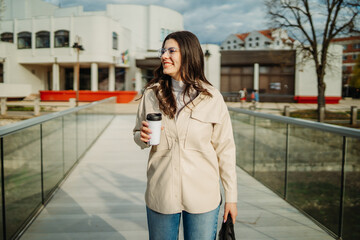 Naklejka premium Young caucasian woman walk home from work drink coffee and use smartphone 