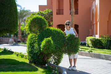 A woman stands in front of a green bush that looks like an elephant