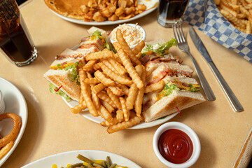 classic club sandwich platter featuring layers of toasted white bread filled with ham, cheese, crispy bacon, lettuce, tomato, and mayonnaise. crinkle-cut French fries and a side of creamy coleslaw,