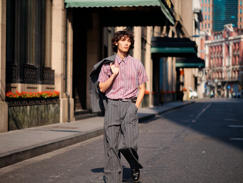 Portrait of handsome Chinese young man wearing gray suit walking in the street, young guy with black curly hair with urban background. Male fashion, cool Asian young man lifestyle.