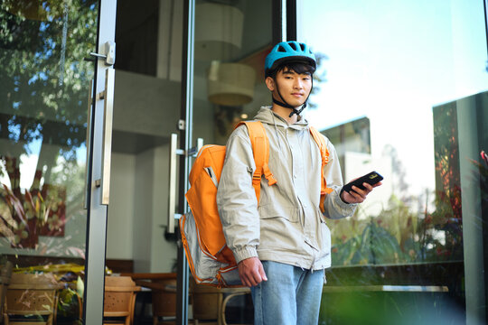 Asian delivery guy walking out of the restaurant while on his phone.