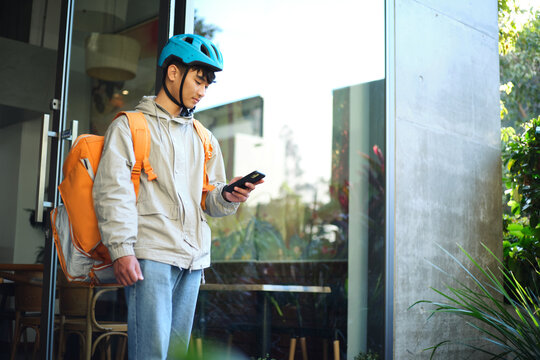 Asian delivery guy walking out of the restaurant while on his phone