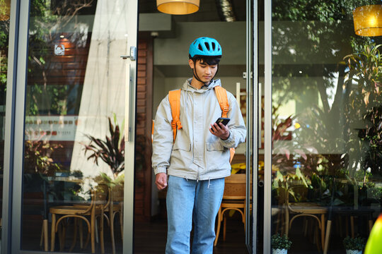 Asian delivery guy walking out of the restaurant while on his phone
