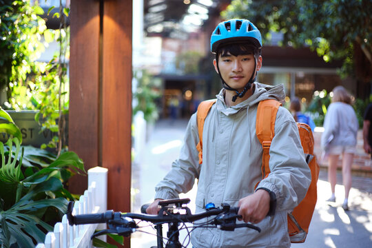 Asian delivery rider walking with his bicycle