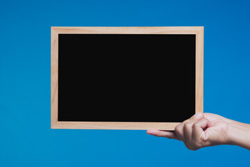Hand holding blank blackboard with wooden frame on blue background for message or announcement.
