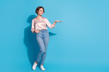 Confident young woman in stylish pink satin blouse against blue background displaying open hand gesture