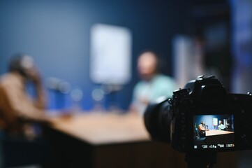 Focus on the camera filming the men's podcast in a professional podcast studio.